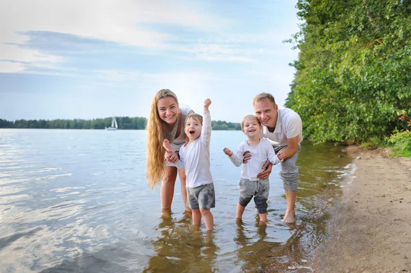 Familia feliz - padre, madre, dos hijos en la playa con los pies en el agua al atardecer —  Fotos de Stock