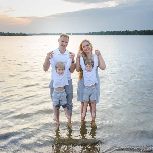 Glückliche Familie - Vater, Mutter, zwei Söhne am Strand mit den Füßen im Wasser bei Sonnenuntergang — Stockfoto