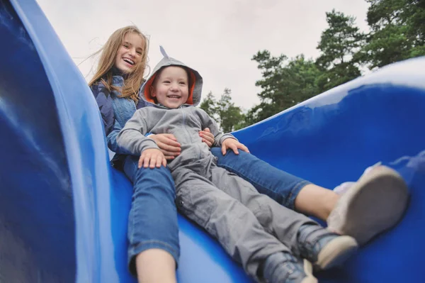 Усміхнена дівчина і хлопчик розважаються на дитячому слайді — стокове фото