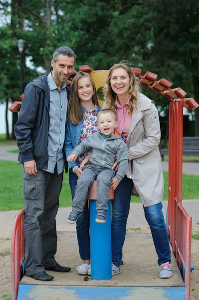 Famiglia positiva madre e padre con figlio e figlia che giocano nel parco giochi — Foto Stock