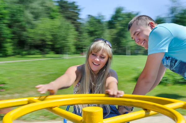 Jovem casal se divertindo no carrossel no parque infantil — Fotografia de Stock