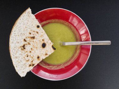 Kırmızı bir kabın içinde yeşil mercimek çorbası