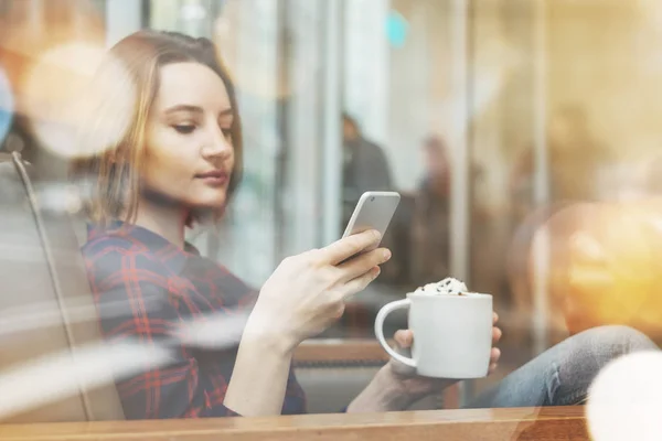 魅力的な笑みを浮かべて内気な少女、居心地の良いコーヒー ショップに座っている彼女の携帯電話の良いニュースが届いた — ストック写真