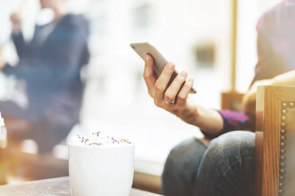 Gros plan de la main féminine tenant téléphone intelligent moderne au café confortable tôt le matin — Photo