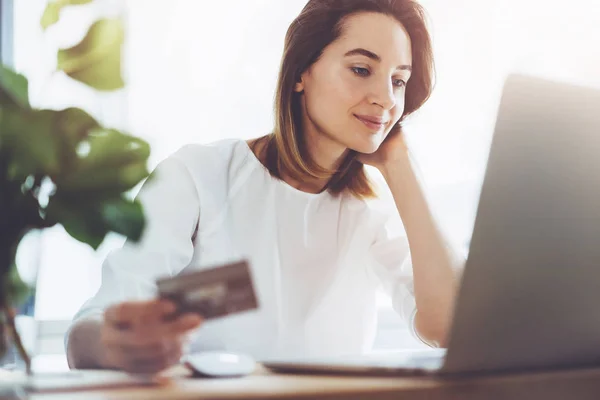 Souriant jeune fille tenant carte de crédit dorée sur les mains et en utilisant pour les achats en ligne de la maison — Photo