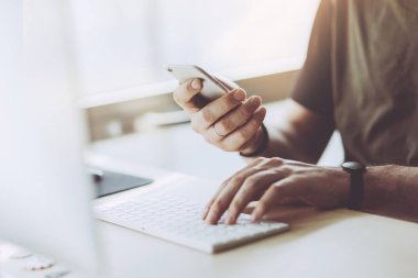 Modern cep telefonunda güneşli ofiste çalışan adam