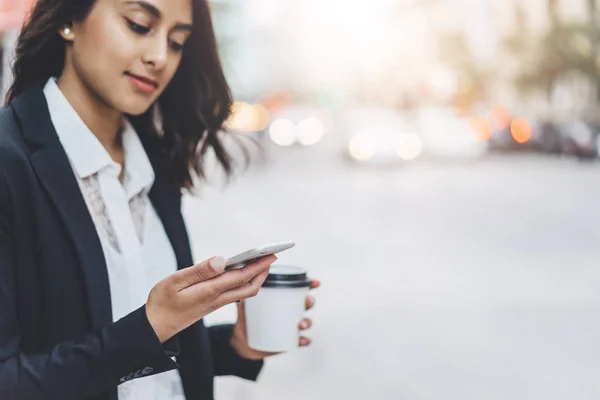 Närbild av kvinnliga händer som håller kaffe att gå och använda smartphone på kvällen utanför — Stockfoto