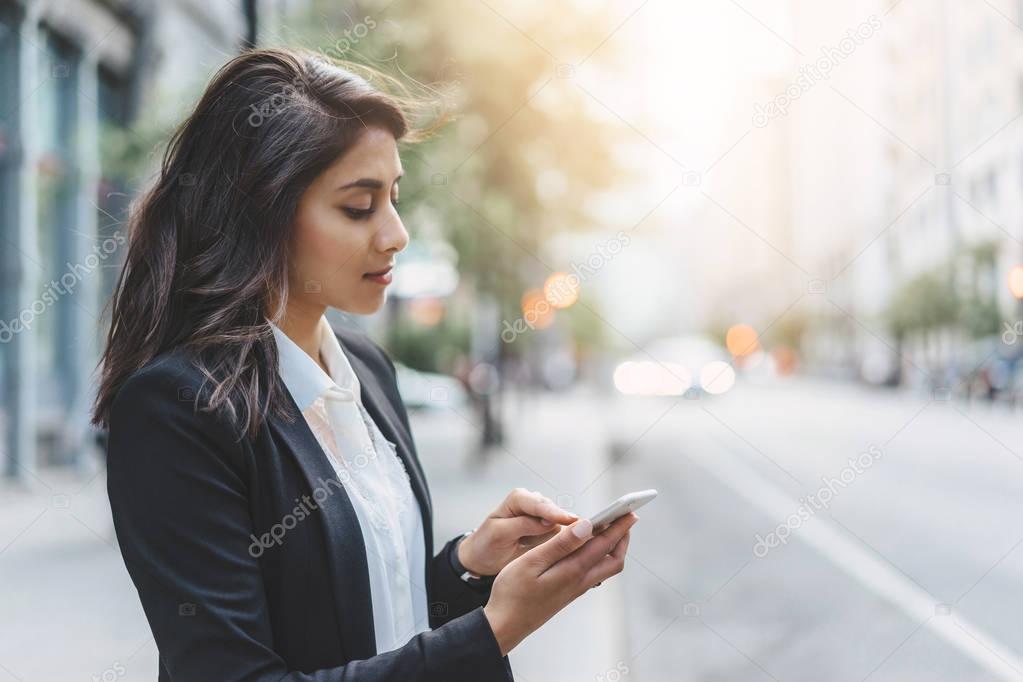 Young business woman wearing black modern suit and using smartphone while coffee break