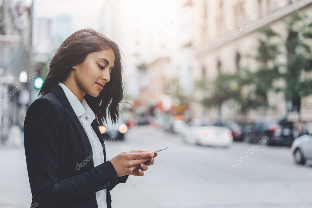 Beautiful woman answering to messages via cell phone while walking on city center