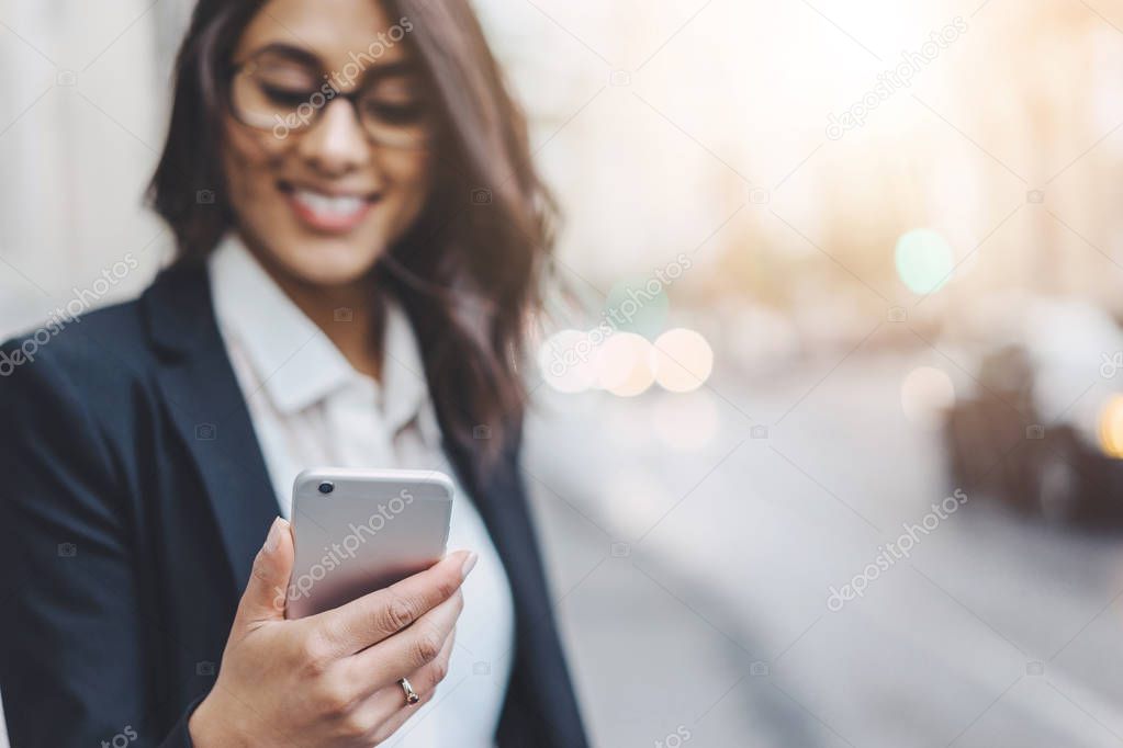 Close-up of professional business woman in black jacket using smartphone while working on new project 