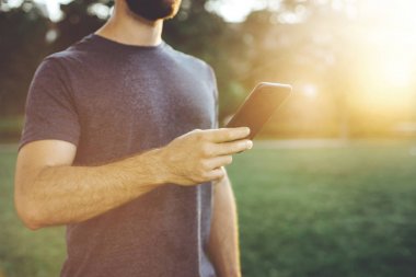 Kaslı adam akıllı telefon uygulama iyi egzersiz oturum sonra Şehir Parkı güneşli sabah programında eğitim denetimi