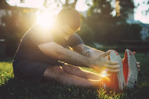 Felice giovane uomo che si estende nel parco prima di correre al tramonto — Foto Stock