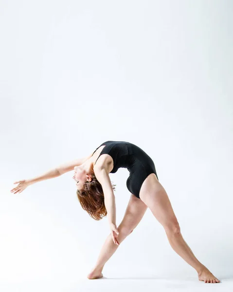 Jeune femme flexible se penche vers l'arrière tout en dansant en justaucorps noir . — Photo
