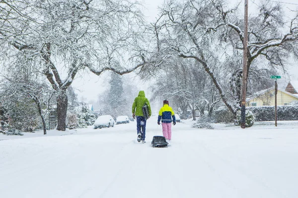 Kinder laufen durch die Mitte einer leeren Straße und schleppen Schlitten im frisch gefallenen Schnee. — Stockfoto