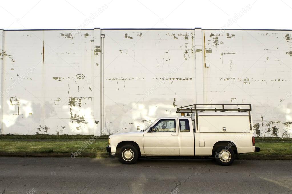 Old pick up truck with canopy and roof rack parked next to a dingy white brick wall. 