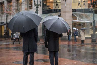 Bir kentsel ortamda yağmurda şemsiye altında iki iş adamı