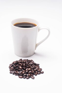 White coffee mug filled with coffee behind a pile of oranic coffee beans. clipart