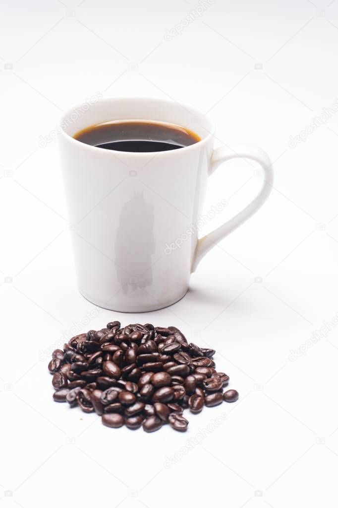 White coffee mug filled with coffee behind a pile of oranic coffee beans.