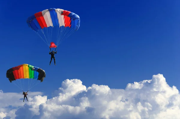 Dos paracaidistas se elevan en paracaídas coloridos a través del cielo azul sin límites contra el fondo de nubes blancas esponjosas —  Fotos de Stock