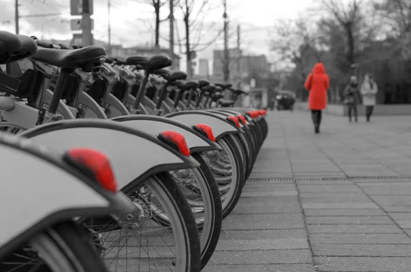 A lonely girl in a red coat takes a walk along a city street along a row of parked bicycles