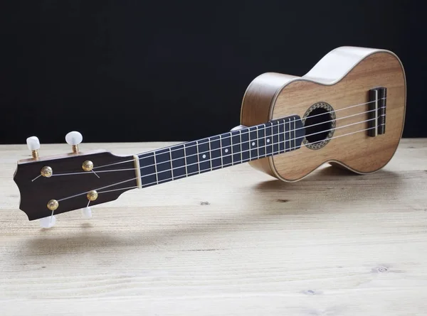 Ukelele op houten bureau op zwarte achtergrond — Stockfoto