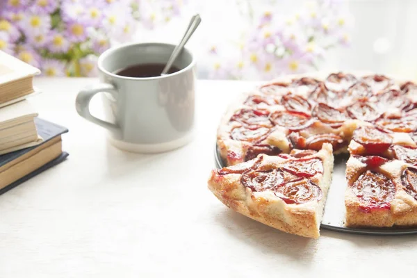 Hela plommon tårta med te mugg, böcker och blommor. — Stockfoto