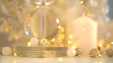 Beyaz ve altın renkli Noel süslemeleri, arka planda parlayan bokeh ışıkları. Küçük topları olan güzel bir yeni yıl ağacı. Beyaz mumlar ve sarı çelenklerle dolu bir ev