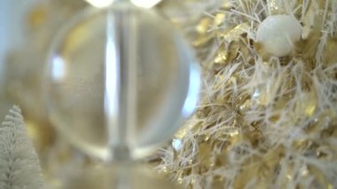 Beyaz ve altın renkli Noel süslemeleri, arka planda parlayan bokeh ışıkları. Küçük topları olan güzel bir yeni yıl ağacı. Beyaz mumlar ve sarı çelenklerle dolu bir ev