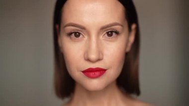 Stüdyoda kameraya bakan gülümseyen kadın portresi. Beyaz arka planda gülümseyen çekici, kendine güvenen esmer kadın. Kadın doğal güzelliği. Yavaş çekim videosu