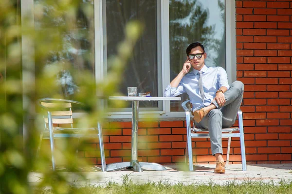 Jóképű férfi napszemüveg beszél a telefonon, ül egy széken, a vidéken — Stock Fotó