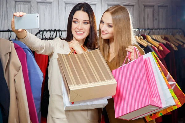 Retrato de moda de duas mulheres bonitas jovens amigos em shopping center com um monte de sacos de compras. A fazer selfie. Sorrindo e feliz depois de fazer compras . — Fotografia de Stock