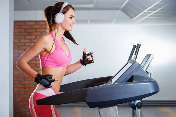 Bir spor kulübünde bir koşu bandı üzerinde çalışan kulaklıklar ile genç gülümseyen kız. Spor ve aktif yaşam tarzları kavramı.
