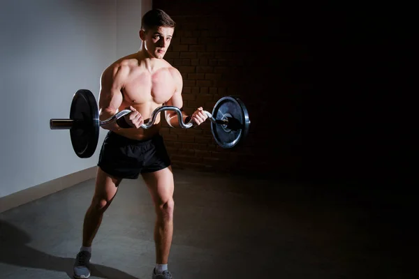Мускулистый мужчина тренируется в спортзале, делает упражнения с штангой, сильный мужской обнаженный пресс — стоковое фото