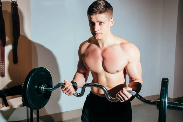 Мускулистый мужчина тренируется в спортзале, делает упражнения с штангой, сильный мужской обнаженный пресс — стоковое фото