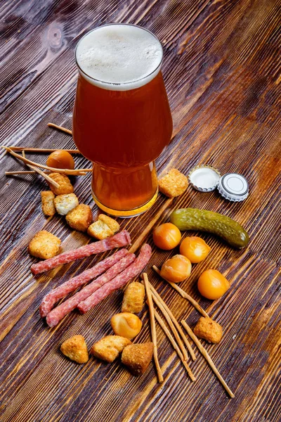 A glass of beer and snacks on a wooden table — Stock Photo, Image