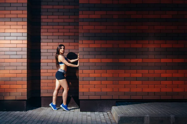 Una giovane donna attraente in abbigliamento sportivo posa su uno sfondo muro di mattoni con copyspace. Formazione all'aperto . — Foto Stock