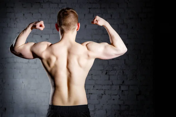 Vista posteriore di giovane attraente uomo bodybuilder muscolare caucasico con corpo perfetto che lavora in centro sportivo, posa, mostrando i muscoli della schiena, concetto di scultura del corpo — Foto Stock