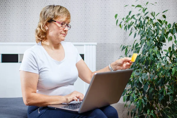 Yaşlılar ve modern teknoloji kavramı. Bir 50s portresi Olgun kadın el kredi kartı, online internet ödeme evde kullanma tutarak. Kapalı üst düzey insanların yaşam tarzı.