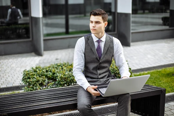Yakışıklı genç işadamı kurumsal bir arka plan açık havada laptop üzerinde bina. 