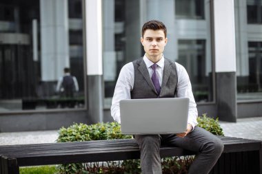 Modern bir şehirde bankta oturmuş bir dizüstü bilgisayar yöneticisi