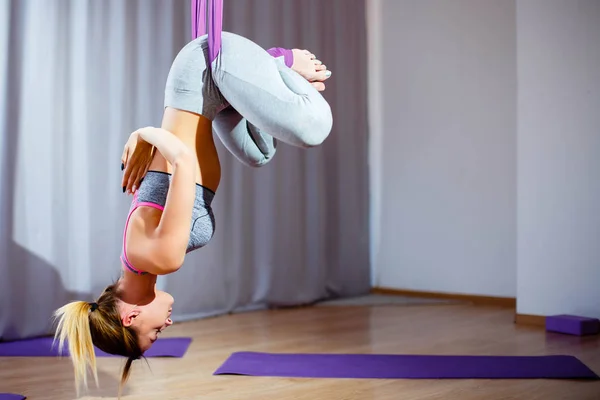 Young woman posing doing aerial yoga exercise with hammock upside down.