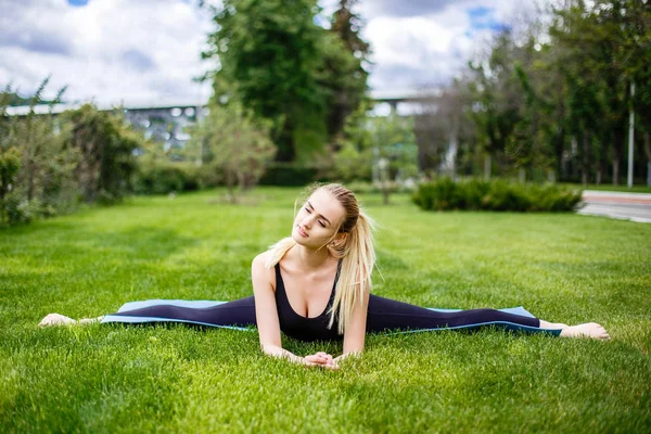 Jovem mulher desportiva sentado na grama no parque, fendas ginástica — Fotografia de Stock
