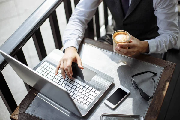 Успешный бизнесмен, работающий в кафе во время кофе-брейка, крупный план рук человека с использованием современного ноутбука в современном стильном кафе — стоковое фото
