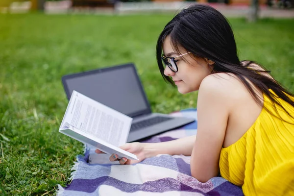 Красивая студентка летом читала книгу и ноутбук на зеленой траве в парке — стоковое фото