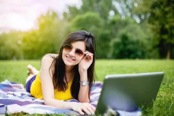 Parkta dizüstü bilgisayarda çalışan mutlu hipster genç kadın