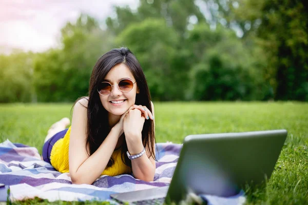 Счастливая студентка-подросток с ноутбуком в кампусе или парке, лежащем на траве — стоковое фото
