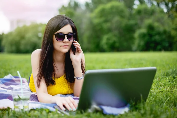 Dizüstü bilgisayarda çalışan ve açık telefonda konuşurken genç kadın.