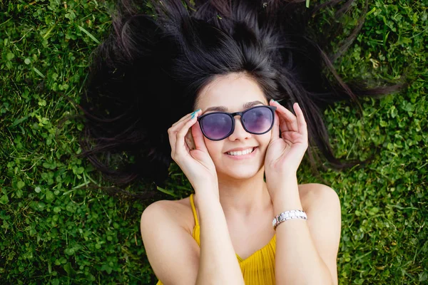Young woman in sunglasses lying on a green lawn and smiling, top view. — Stock Photo, Image
