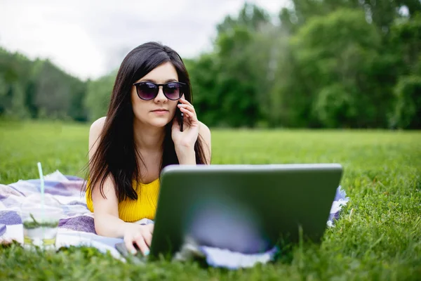Dizüstü bilgisayarda çalışan ve açık telefonda konuşurken genç kadın.