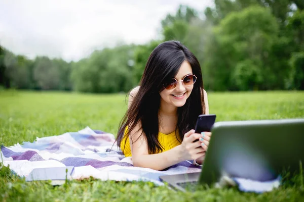 Девушка-студентка разговаривает по телефону, лежит на траве в парке — стоковое фото